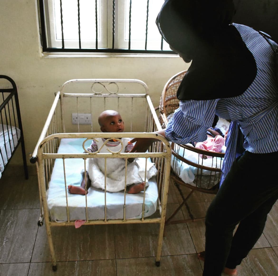Baby in crib with caretaker - Caregiver attending to an infant in a hospital crib